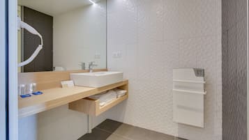 A modern bathroom with a sink, mirror, towel rack, and a towel dispenser.