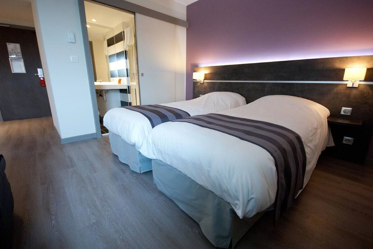 Une chambre d’hôtel avec deux lits, une salle de bain et un miroir.