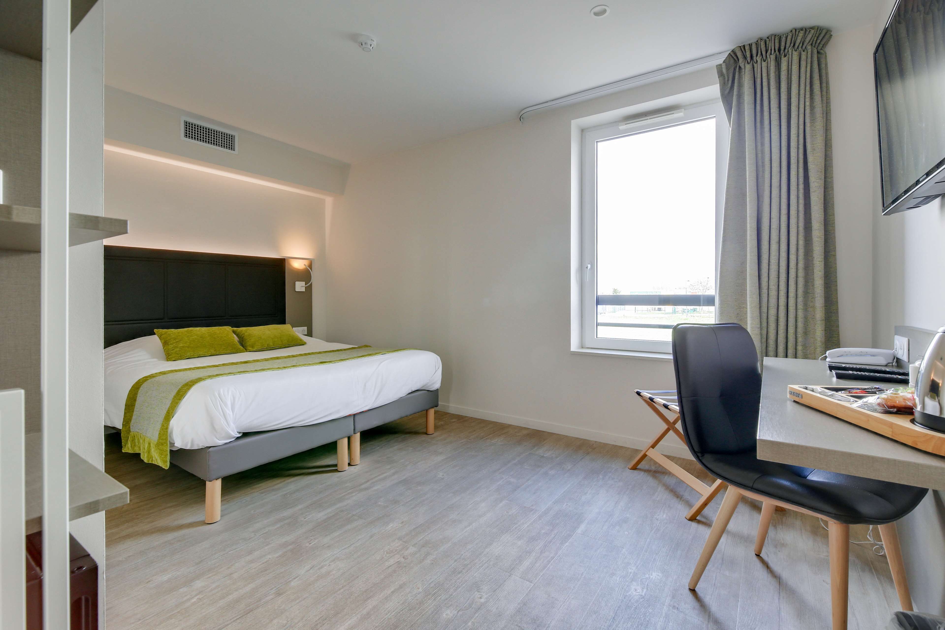 Una habitació d'hotel moderna amb llit, escriptori, cadira i una finestra gran.