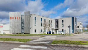 Een modern hotel met een opvallend 'HOTEL' bord, een voetgangersoversteek en een parkeerplaats met auto's.