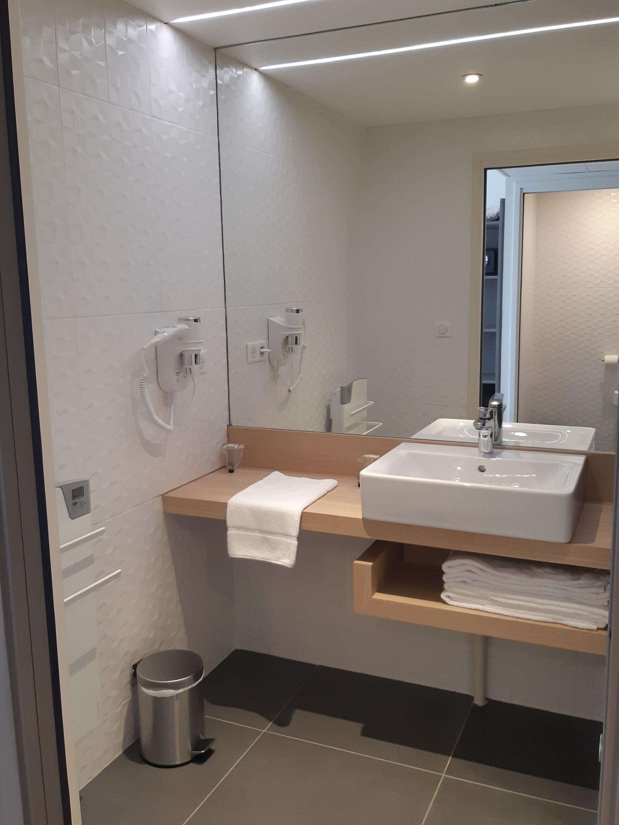 Un baño moderno con dos lavamanos, un perchero, un cubo de basura y un espejo.