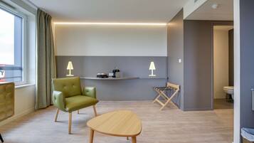 A modern hotel room with a green leather chair, a wooden table, and a small desk with a lamp.