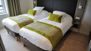 A hotel room with two beds, each with white bedding and green accents, a dark headboard, and a small bedside table with a remote control.