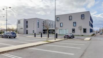 A modern hotel with a flat facade, multiple windows, and a parking lot with several cars.