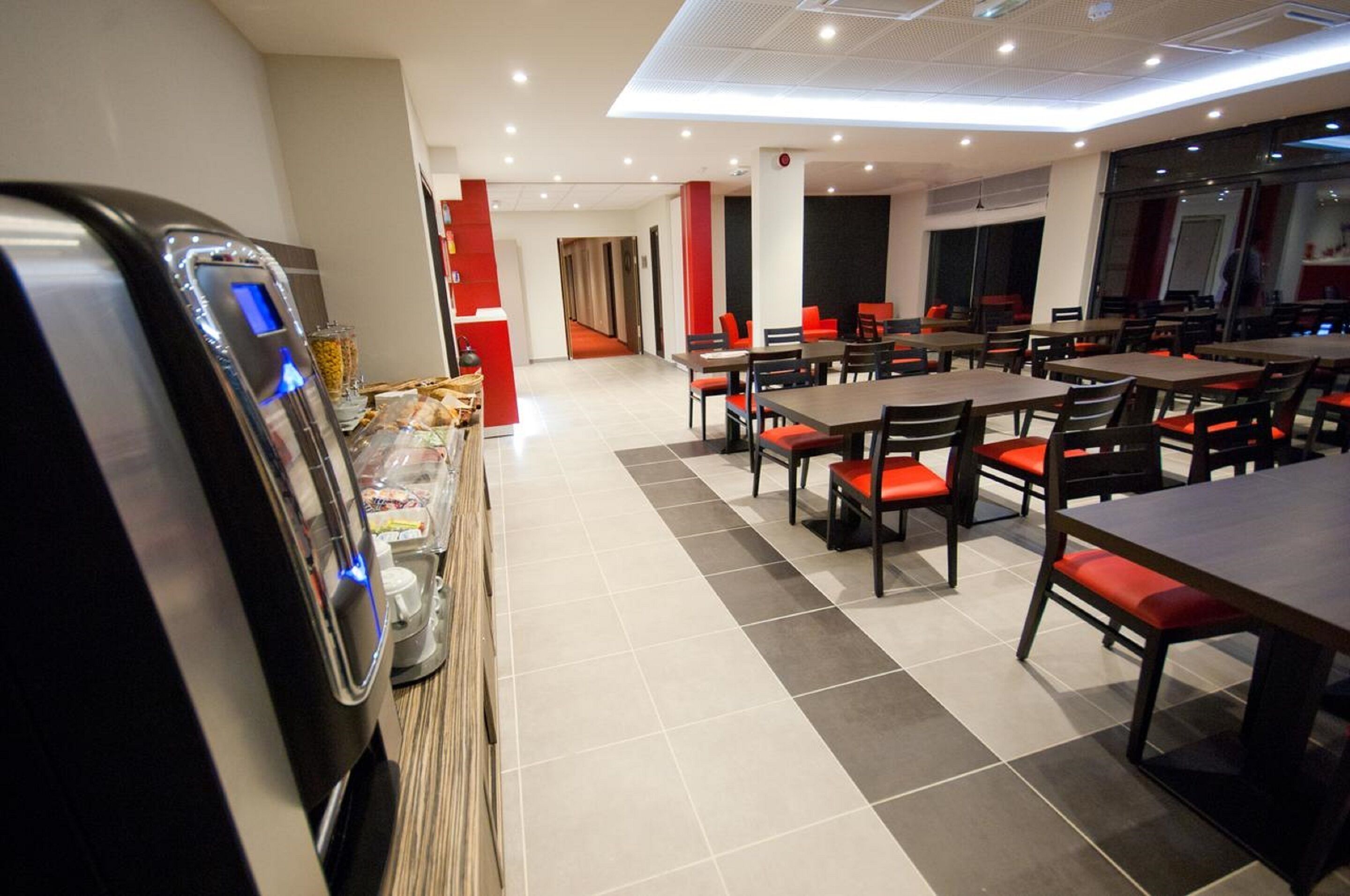 A modern restaurant with multiple tables and chairs, a self-service beverage machine, and a tiled floor.