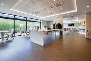 Un vestíbulo de hotel amplio y moderno, con un mostrador de recepción central, zona de estar y grandes ventanales que ofrecen vistas al exterior.