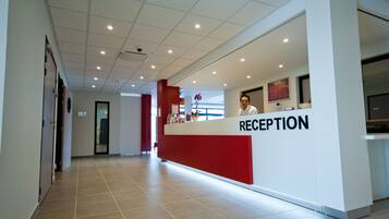 Et receptionsområde med røde og hvide farver, flisegulv og et loft med indbygningsbelysning.