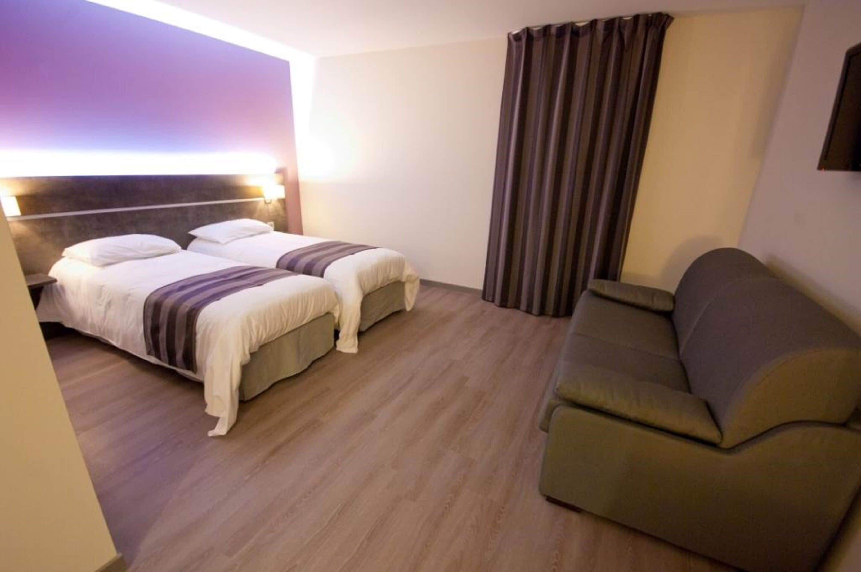 Habitación de hotel con dos camas, un sofá y un ventanal con cortinas.