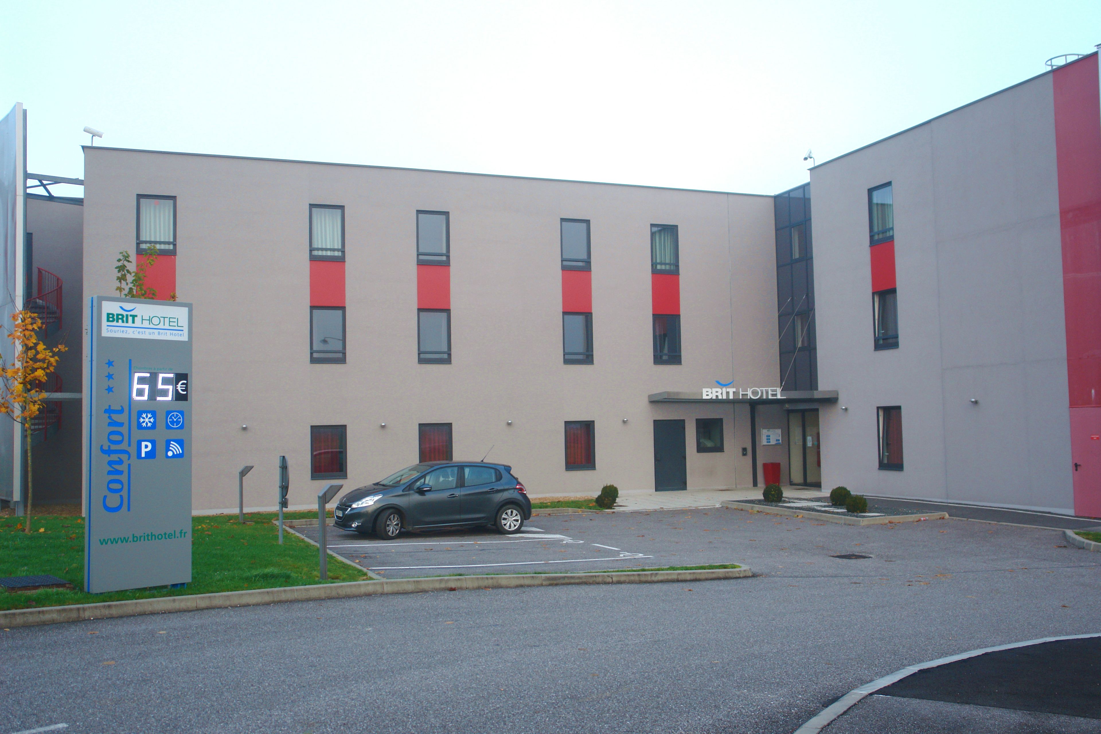 A modern hotel building with a parking lot, a car, and a sign indicating a price of 65 euros.