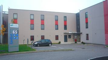 A modern hotel building with a parking lot, a car, and a sign indicating a price of 65 euros.
