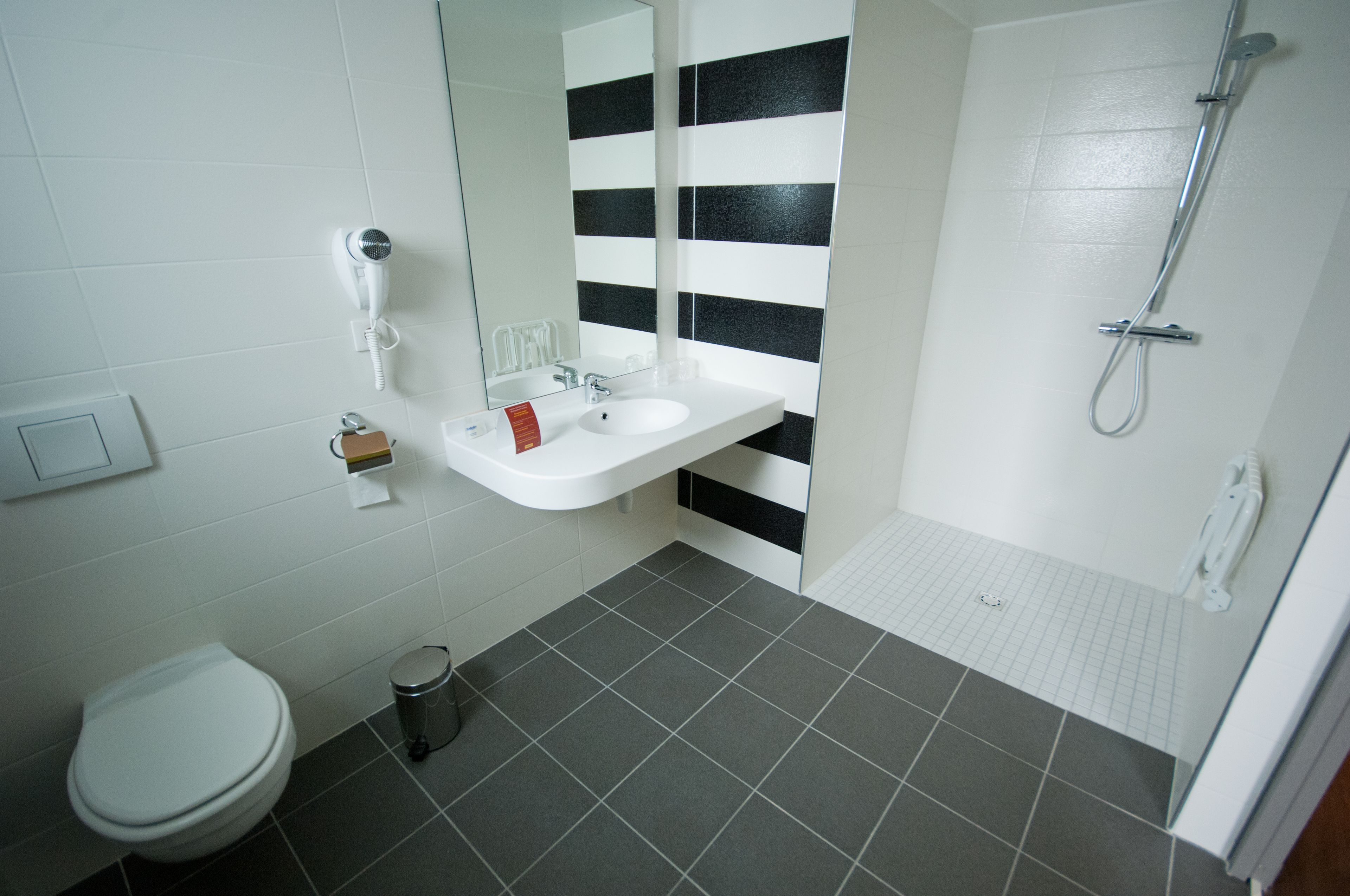 Une salle de bain avec un lavabo blanc, un miroir, des toilettes et une douche.
