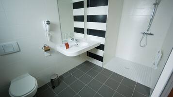 Une salle de bain avec un lavabo blanc, un miroir, des toilettes et une douche.