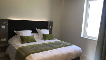 Een moderne slaapkamer met een groot bed, twee nachtkastjes, een hoofdbord en een raam met gordijnen.