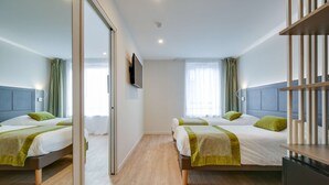 A modern hotel room with two beds, a flat-screen TV, and a wooden floor.
