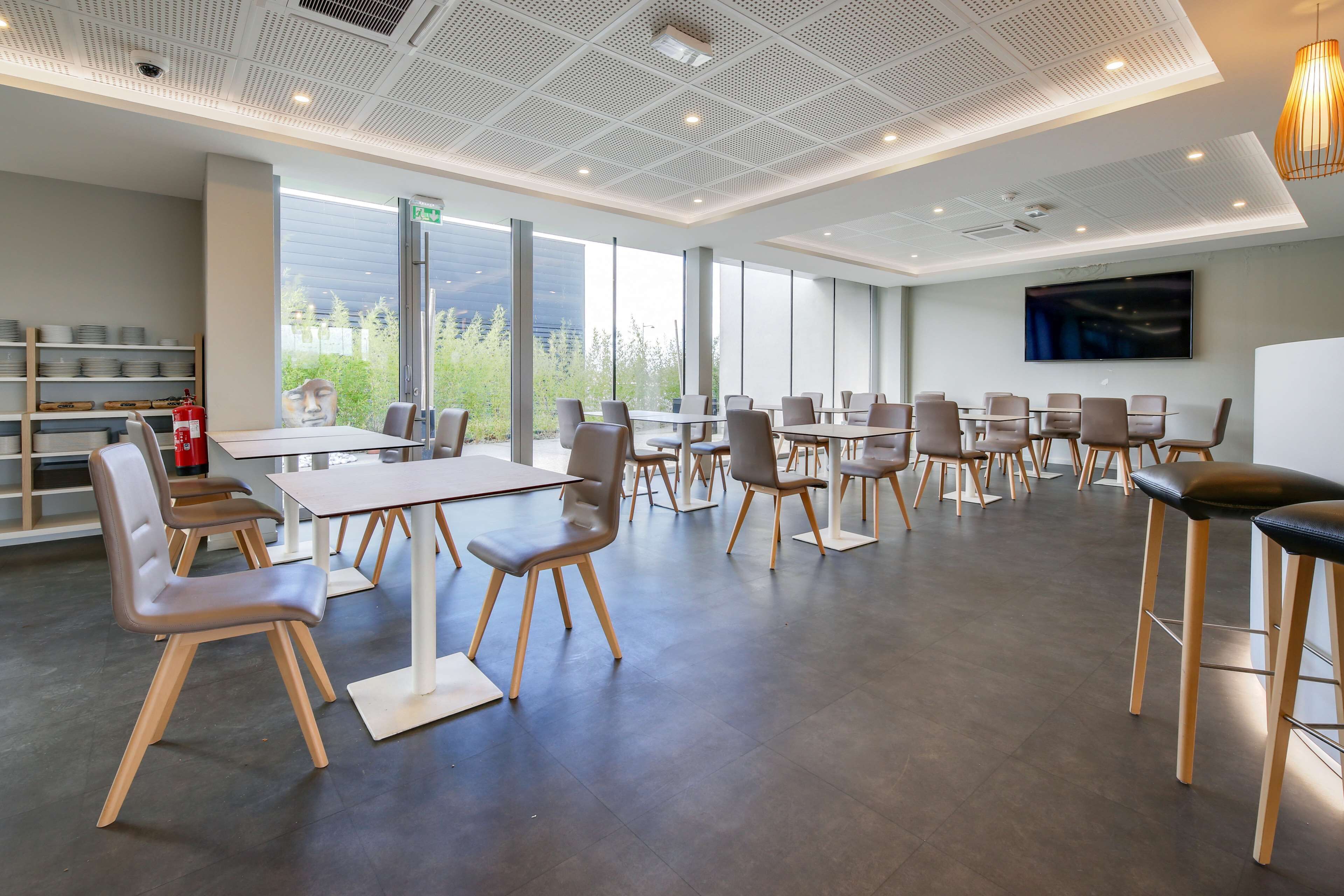 Een moderne congreszaal met grote ramen, een flatscreen televisie en diverse zitmogelijkheden.