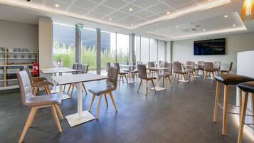 Een moderne congreszaal met grote ramen, een flatscreen televisie en diverse zitmogelijkheden.