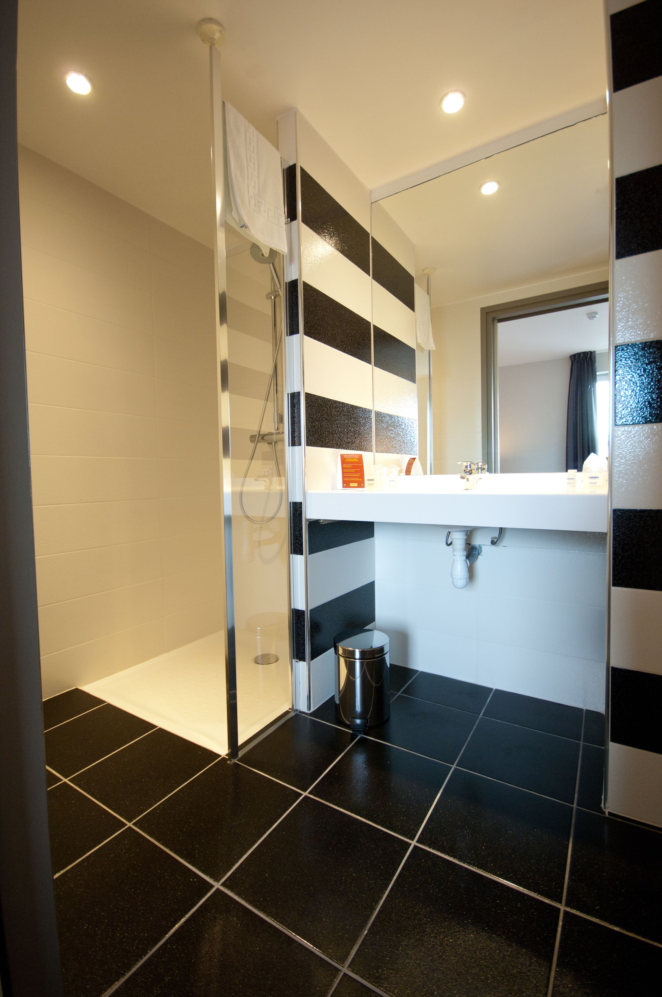 Un baño moderno con cabina de ducha de vidrio, un lavamanos blanco y baldosas a rayas negras y blancas.