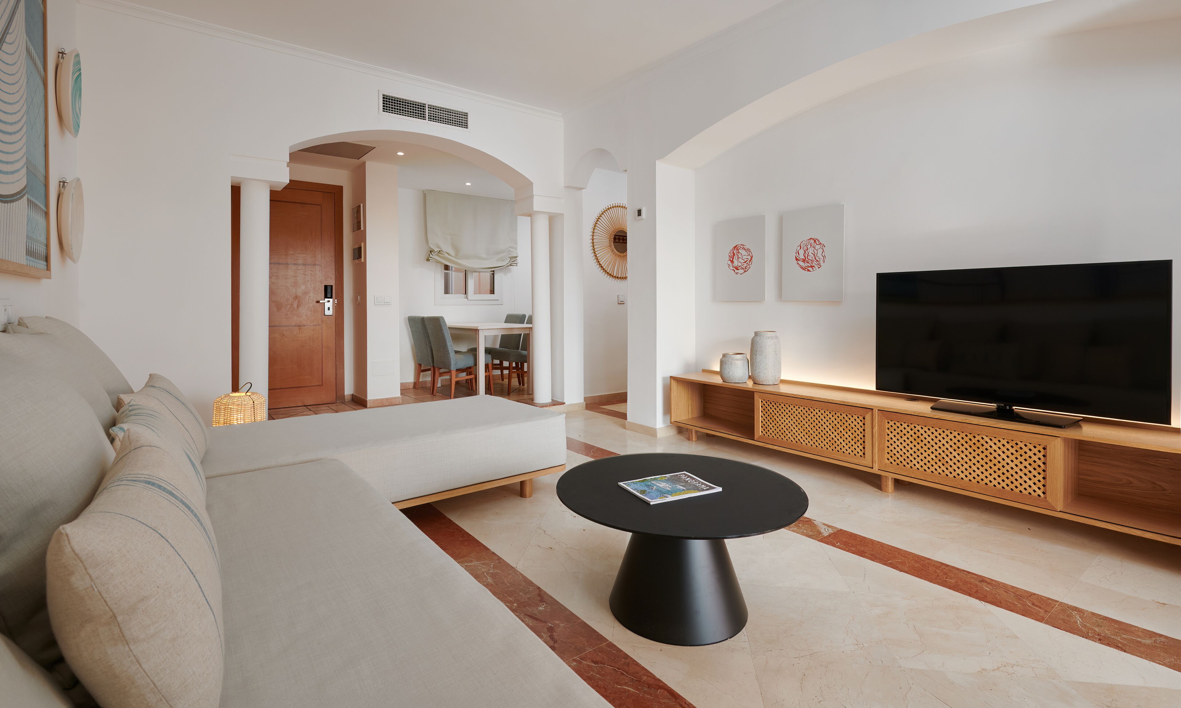 A modern living room with a sofa, a coffee table, a TV, and a dining area with chairs.