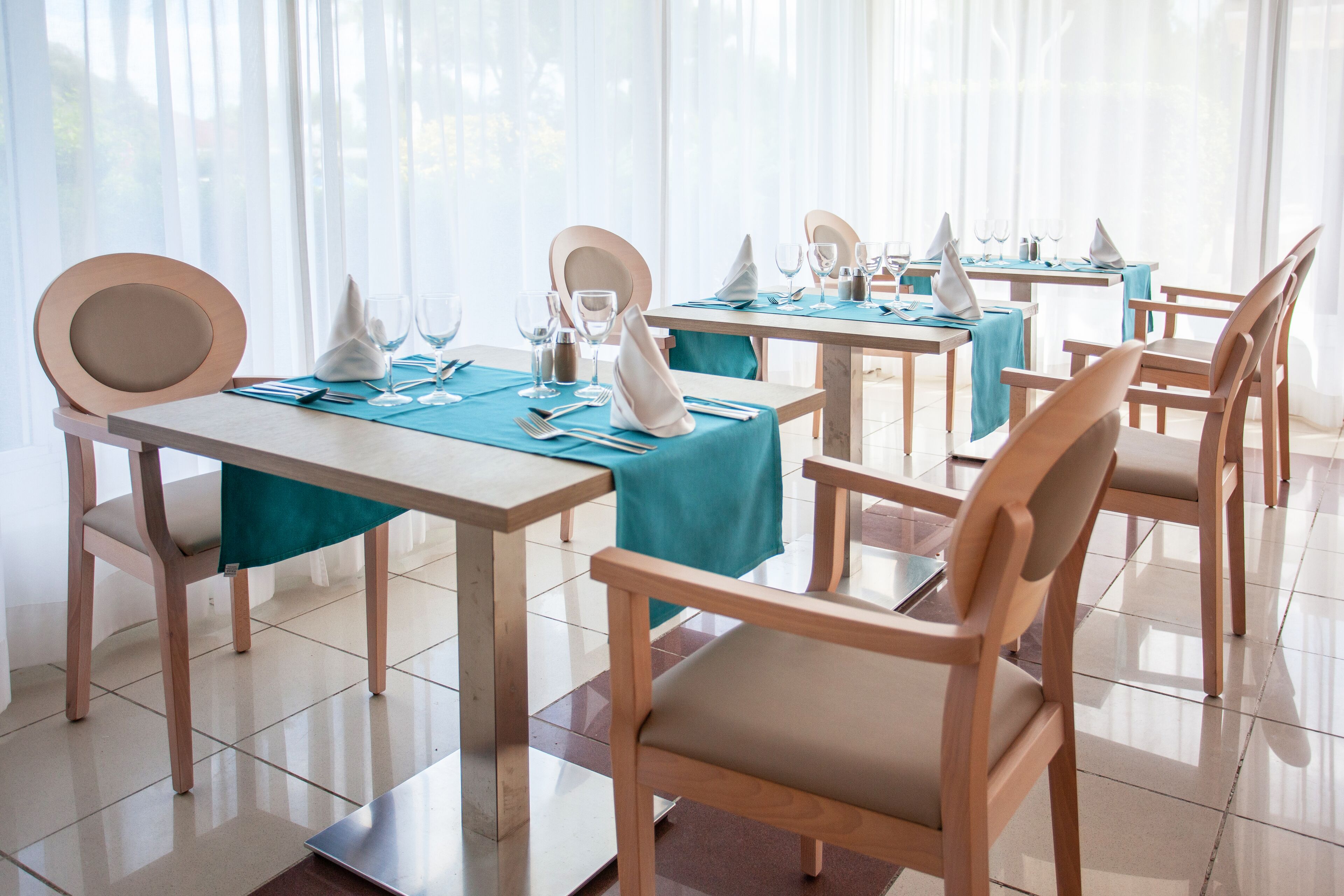 A dining area with tables set for four, each with a tablecloth, chairs, and tableware.