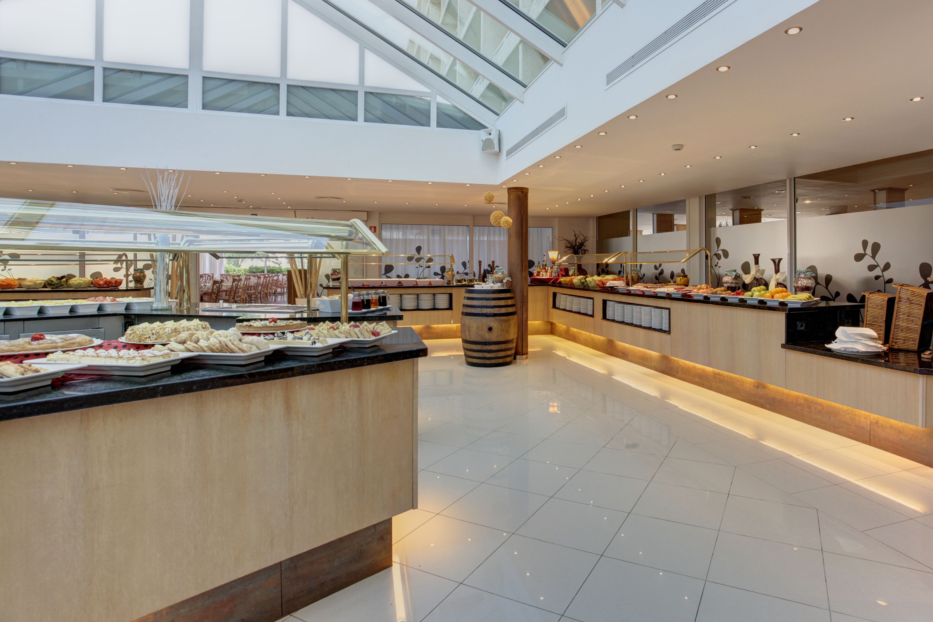 Een moderne hotellobby met een centraal eiland met een buffet, grote ramen en een hoge plafond.