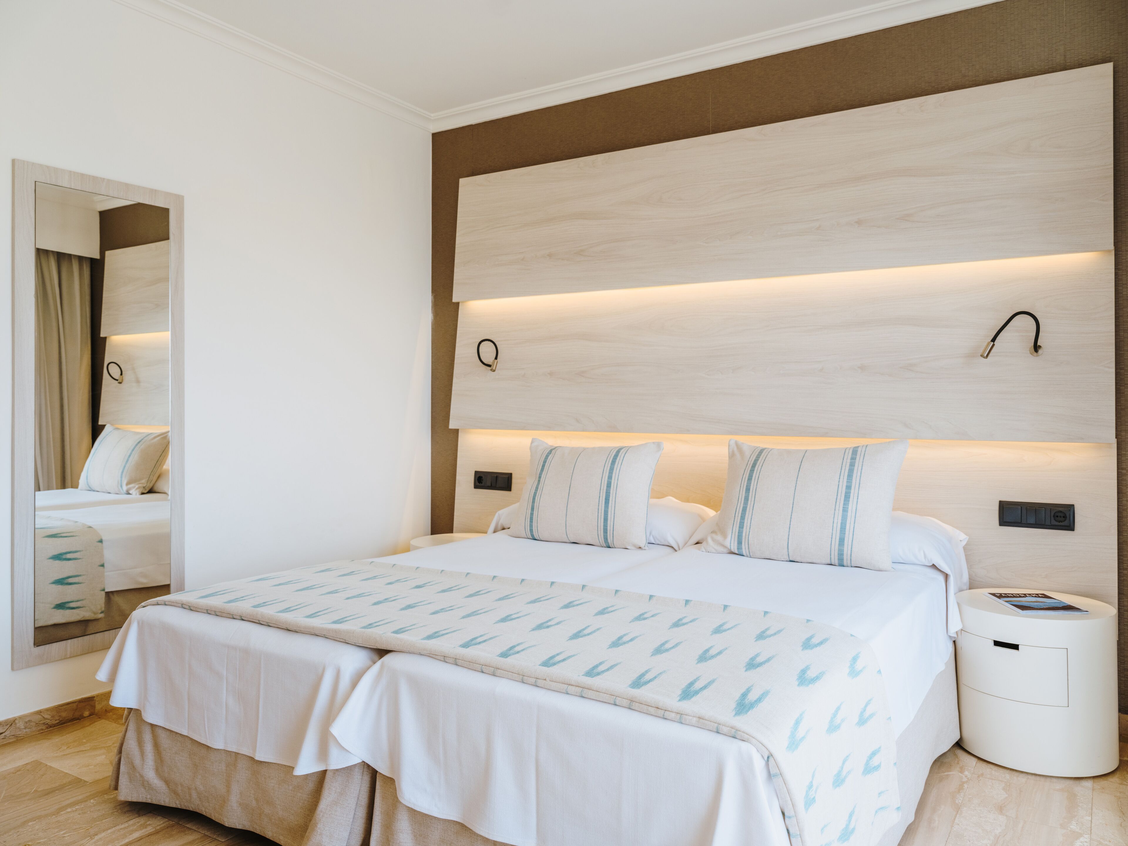 A modern hotel room with a large bed, bedside tables, a mirror, and a nightstand.