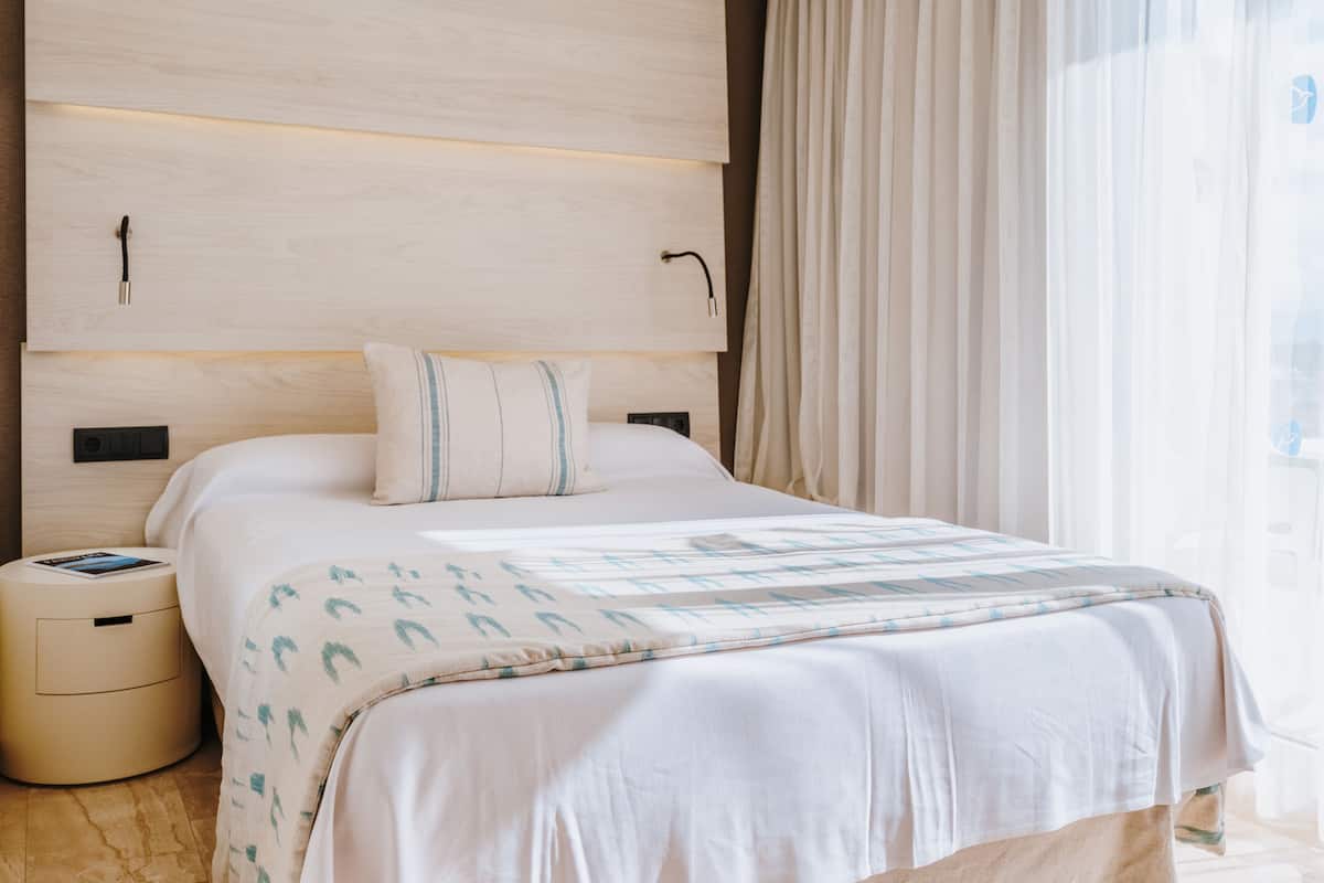 Ein modernes Hotelzimmer mit einem großen Bett, einem Nachttisch, Vorhängen und einem Fenster.
