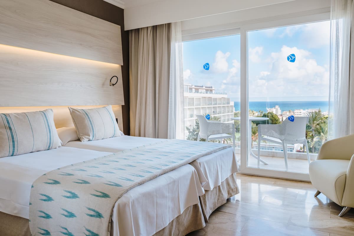 Ein Hotelzimmer mit Bett, einem Sessel und einem Balkon mit Blick auf das Meer und Gebäude.
