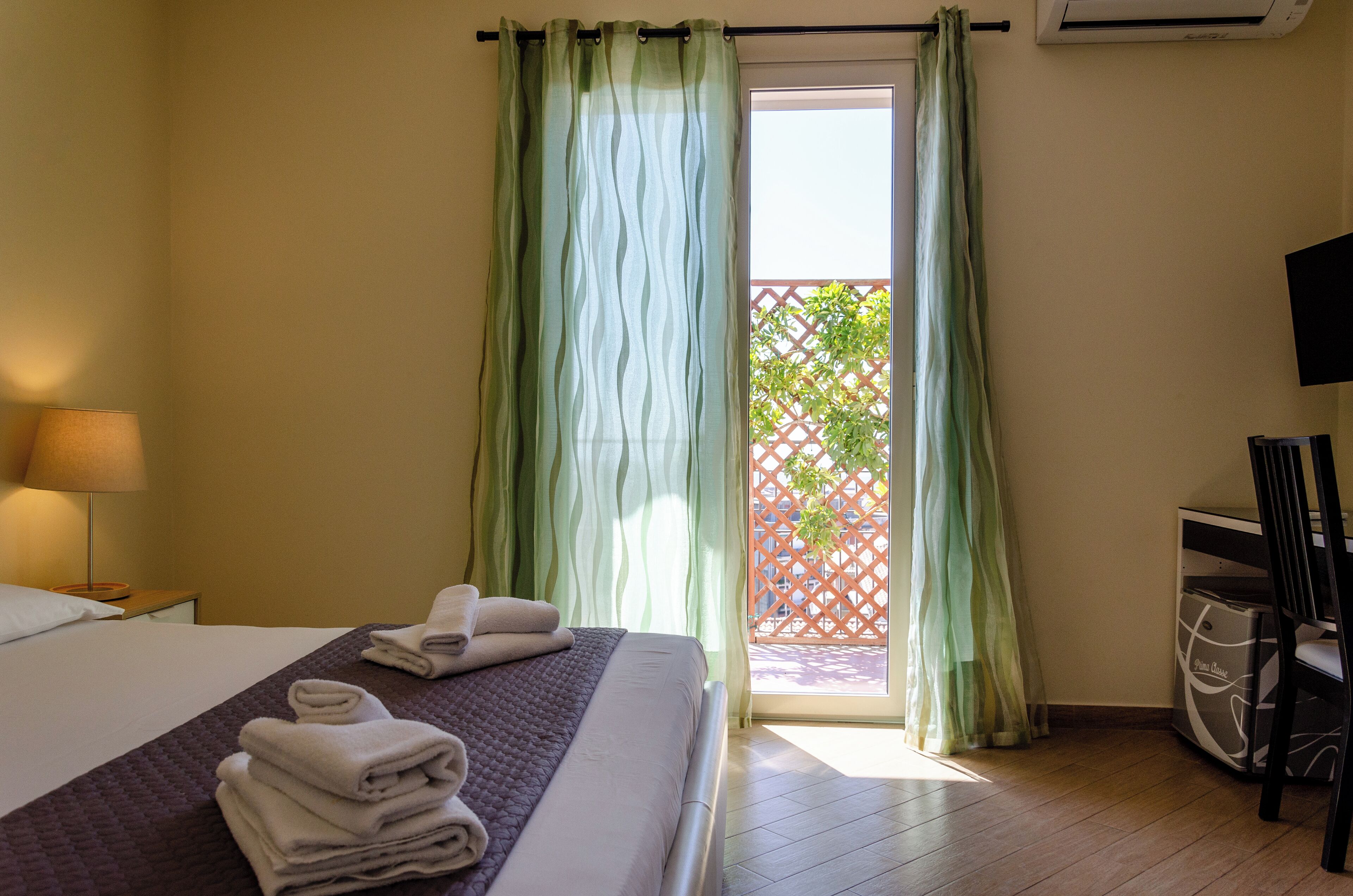 A hotel room with a bed, a lamp, a chair, and a view of a balcony with a lattice fence.