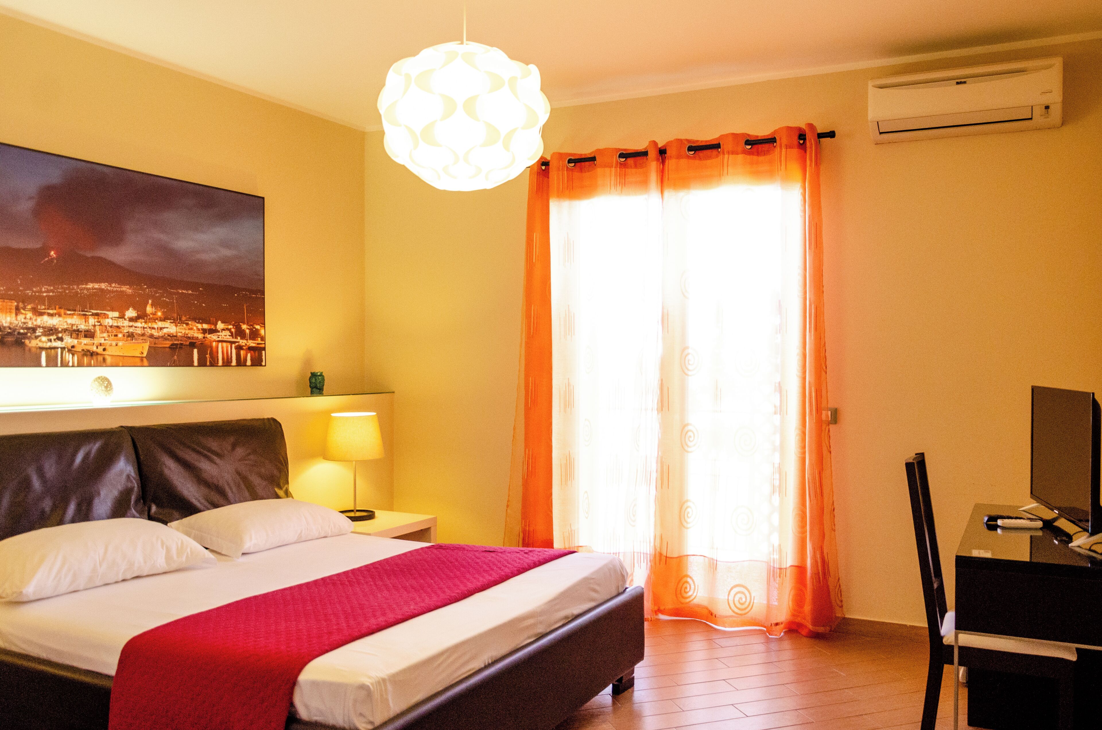 Habitación de hotel con cama, escritorio, aire acondicionado y un ventanal con cortinas.