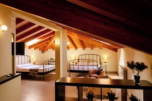 A hotel room with two beds, wooden beams on the ceiling, a small table, and a potted plant. - B&B PrimaClasse (Belpasso)