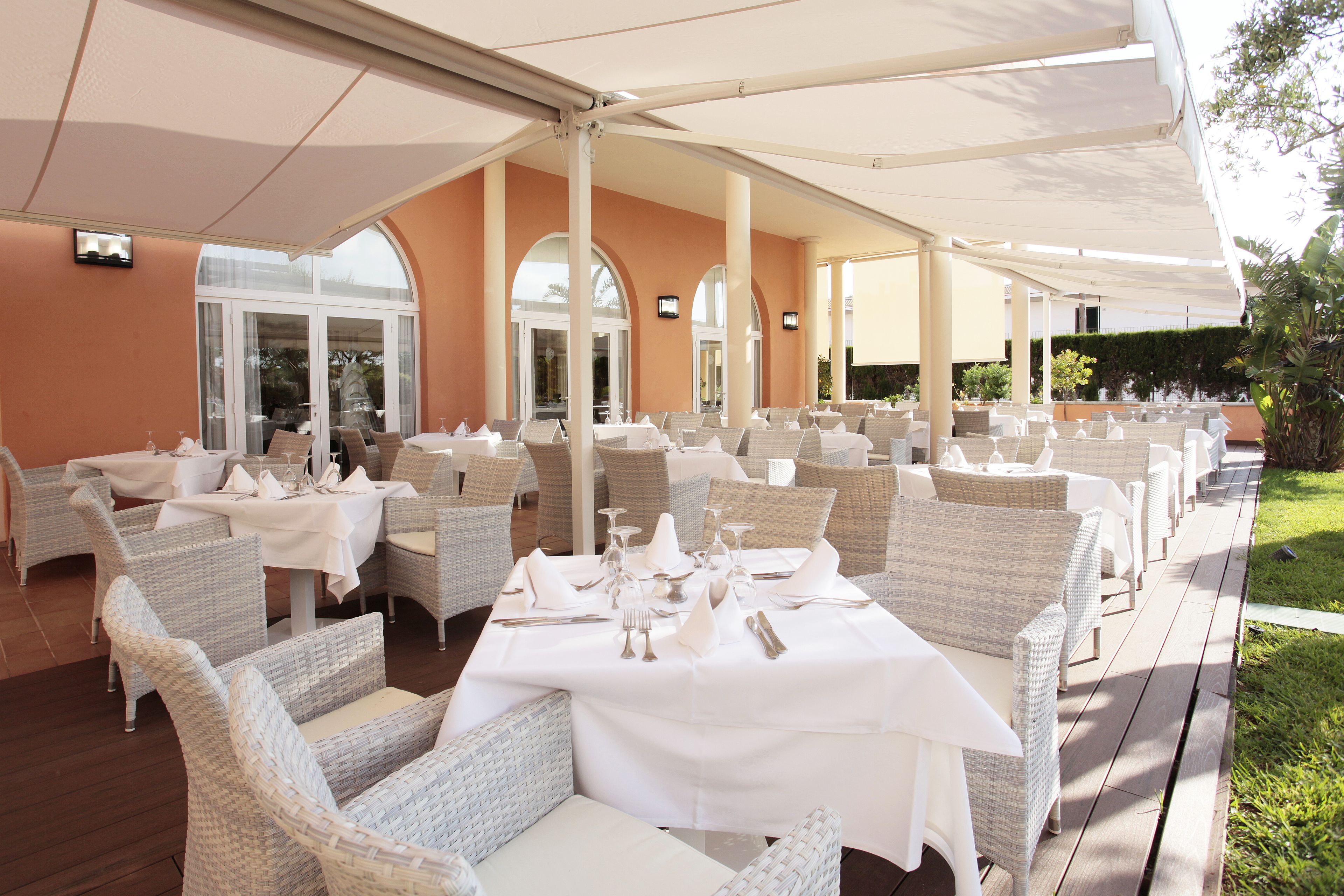 Un espacio de comedor al aire libre con techo, mobiliario de mimbre y manteles blancos.