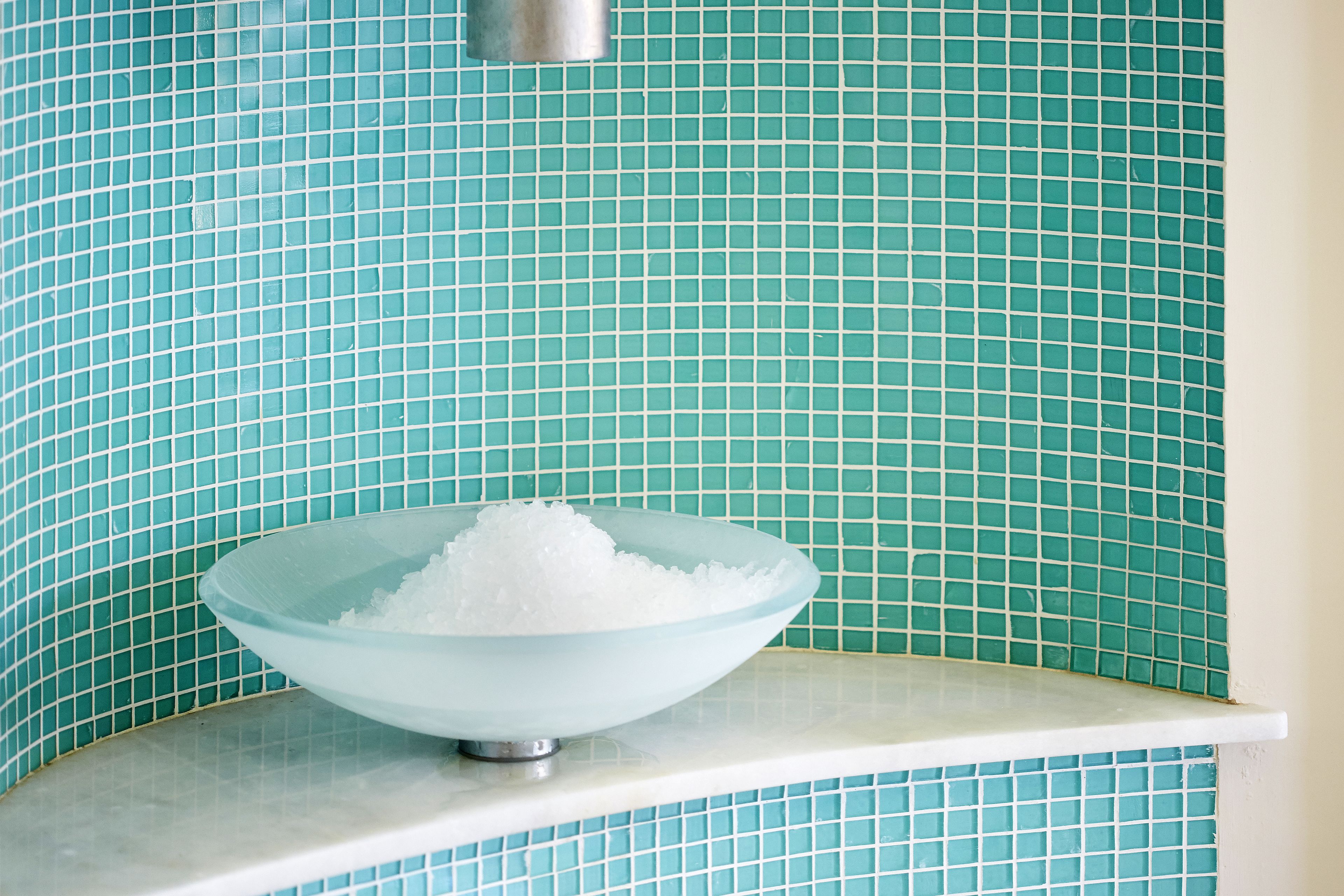 A glass bowl filled with white cubes on a white countertop against a tiled wall.