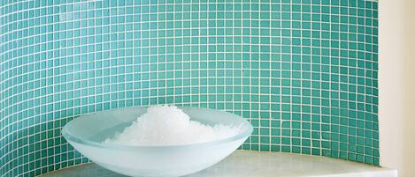 Un cuenco de vidrio lleno de cubos blancos sobre una encimera blanca frente a una pared de azulejos.