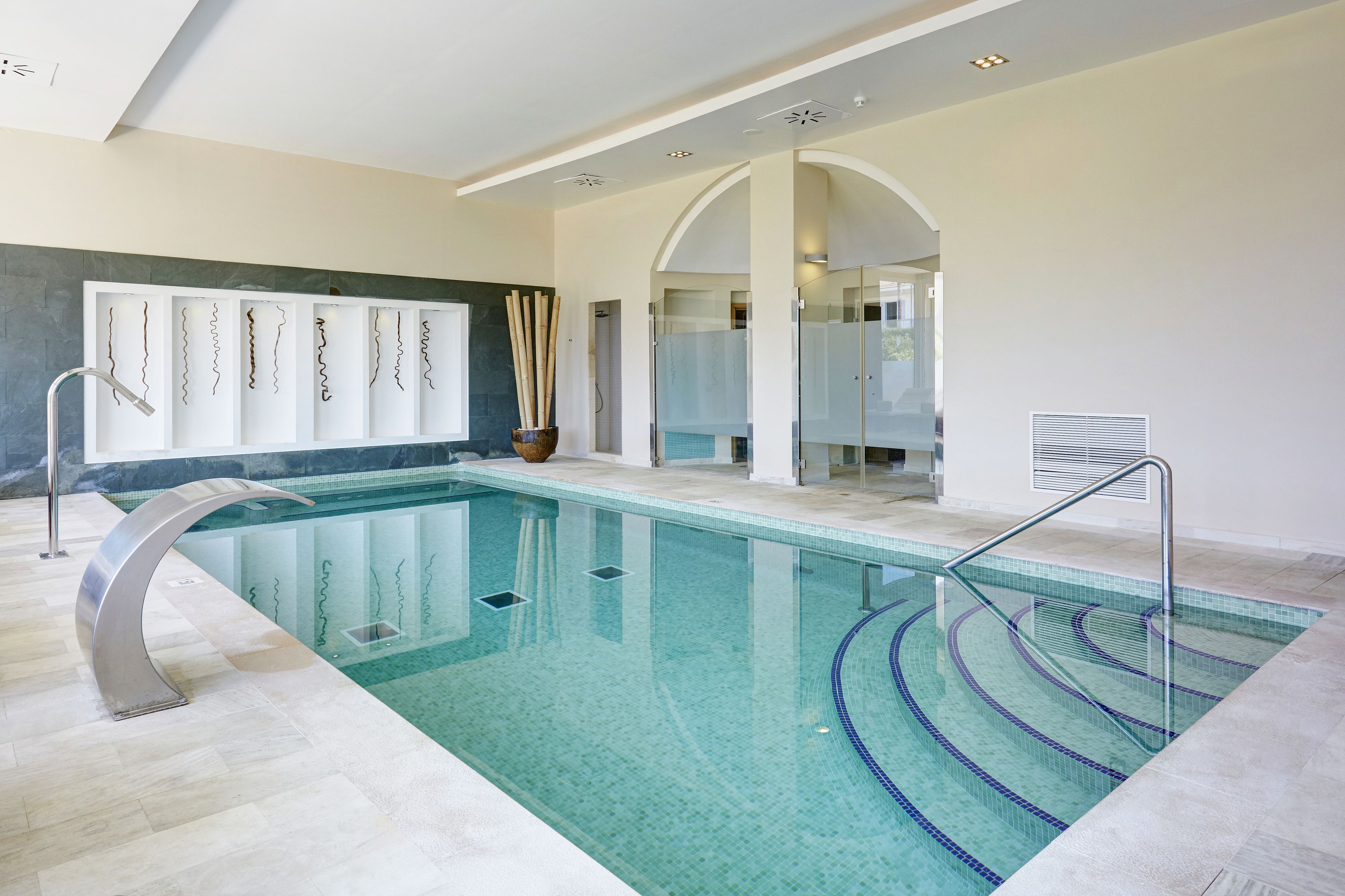 An indoor swimming pool with clear water, a modern design, and a glass-enclosed shower area.