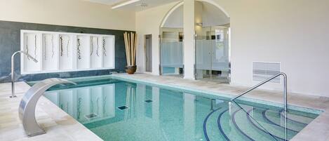 An indoor swimming pool with clear water, a modern design, and a glass-enclosed shower area.