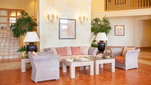 Un salón amplio con un sofá grande, dos sillones y una mesa de centro. Se observan dos plantas en macetas, un cuadro enmarcado en la pared y una escalera al fondo.