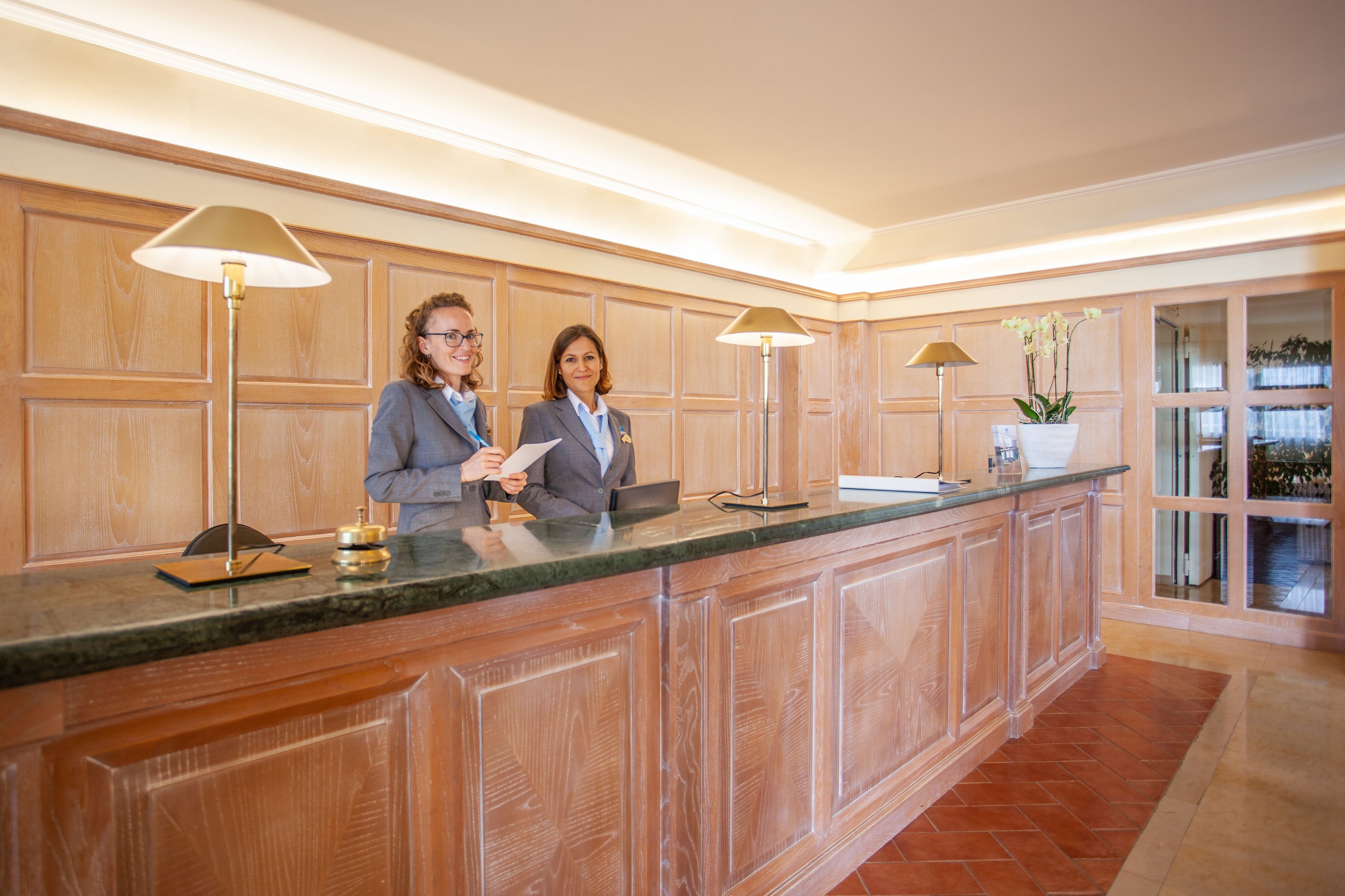 Een receptie met houten lambrisering, een marmeren balie en twee receptionisten.
