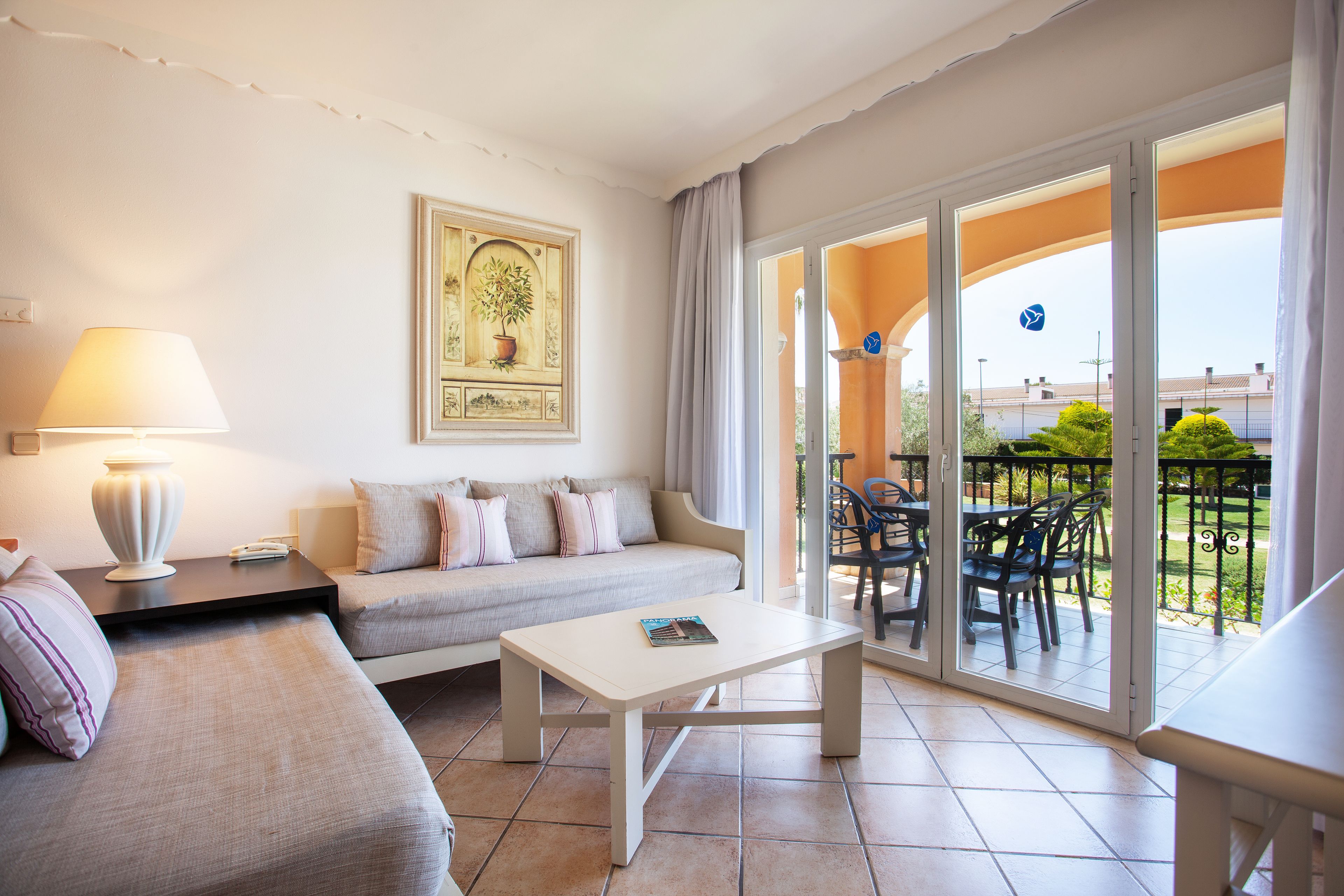 Ein modernes Wohnzimmer mit einer Couch, einem Couchtisch und einer Lampe. Ein Balkon mit Gartenmöbeln und Blick ins Umland.