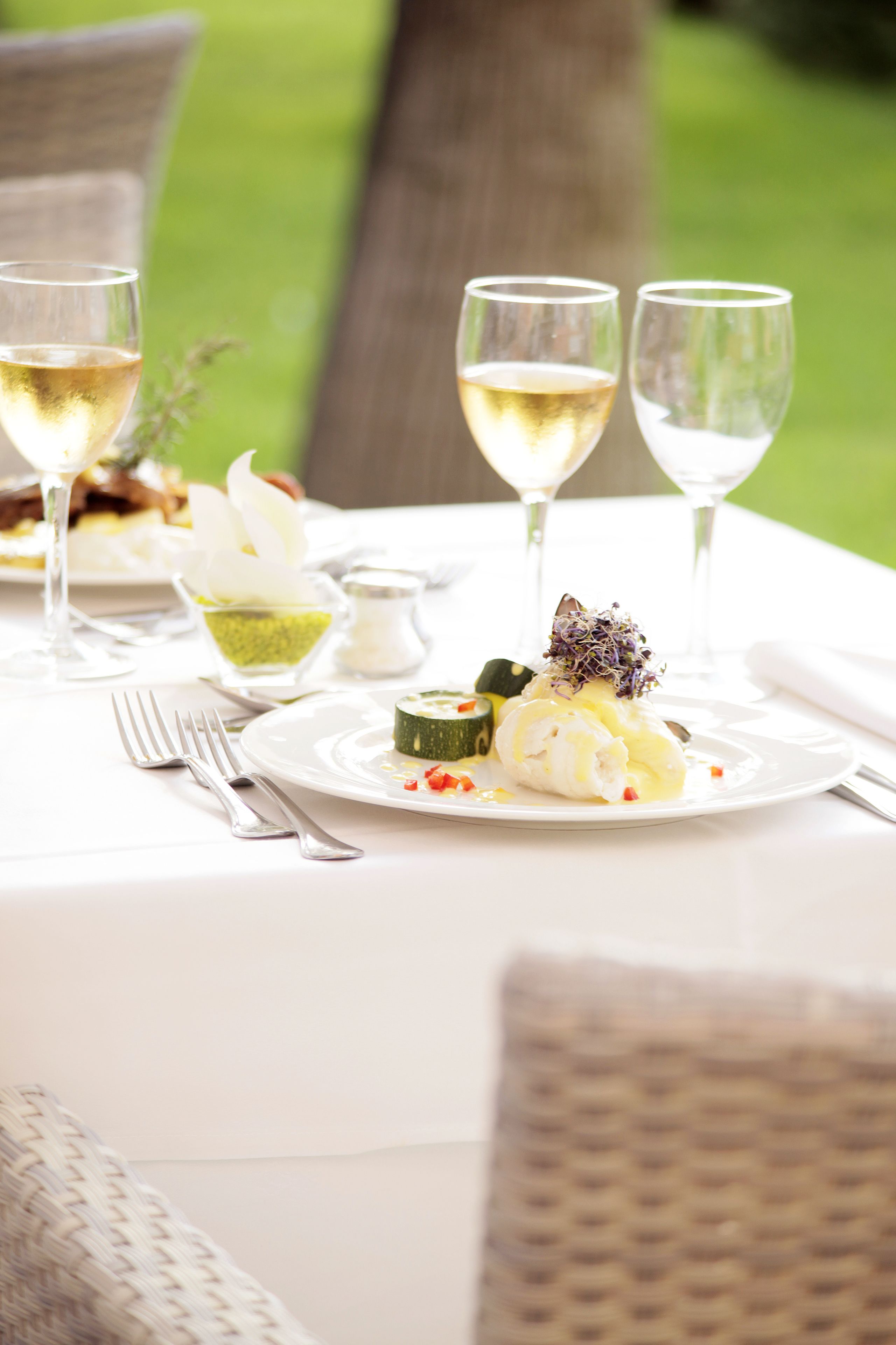 Una mesa lista para una comida, con platos, cubiertos y copas de vino blanco.