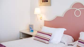 A hotel room with a bed, pillows, a nightstand, a lamp, and a framed picture on the wall.