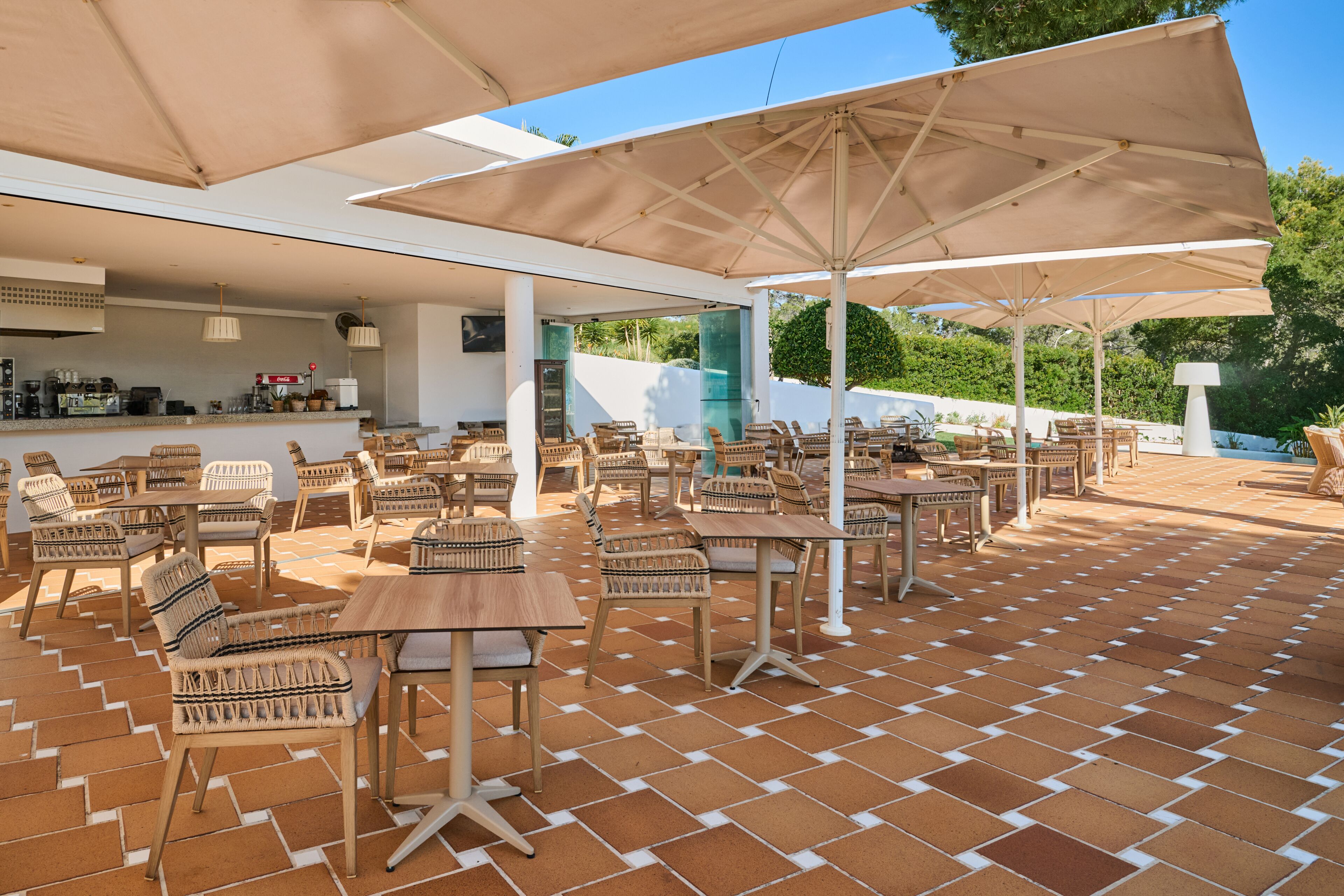 Un espace extérieur aménagé en terrasse, avec des tables et des chaises, des parasols et un coin bar.