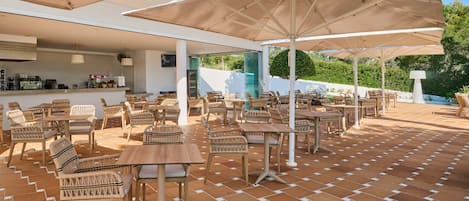 Un espace extérieur aménagé en terrasse, avec des tables et des chaises, des parasols et un coin bar.