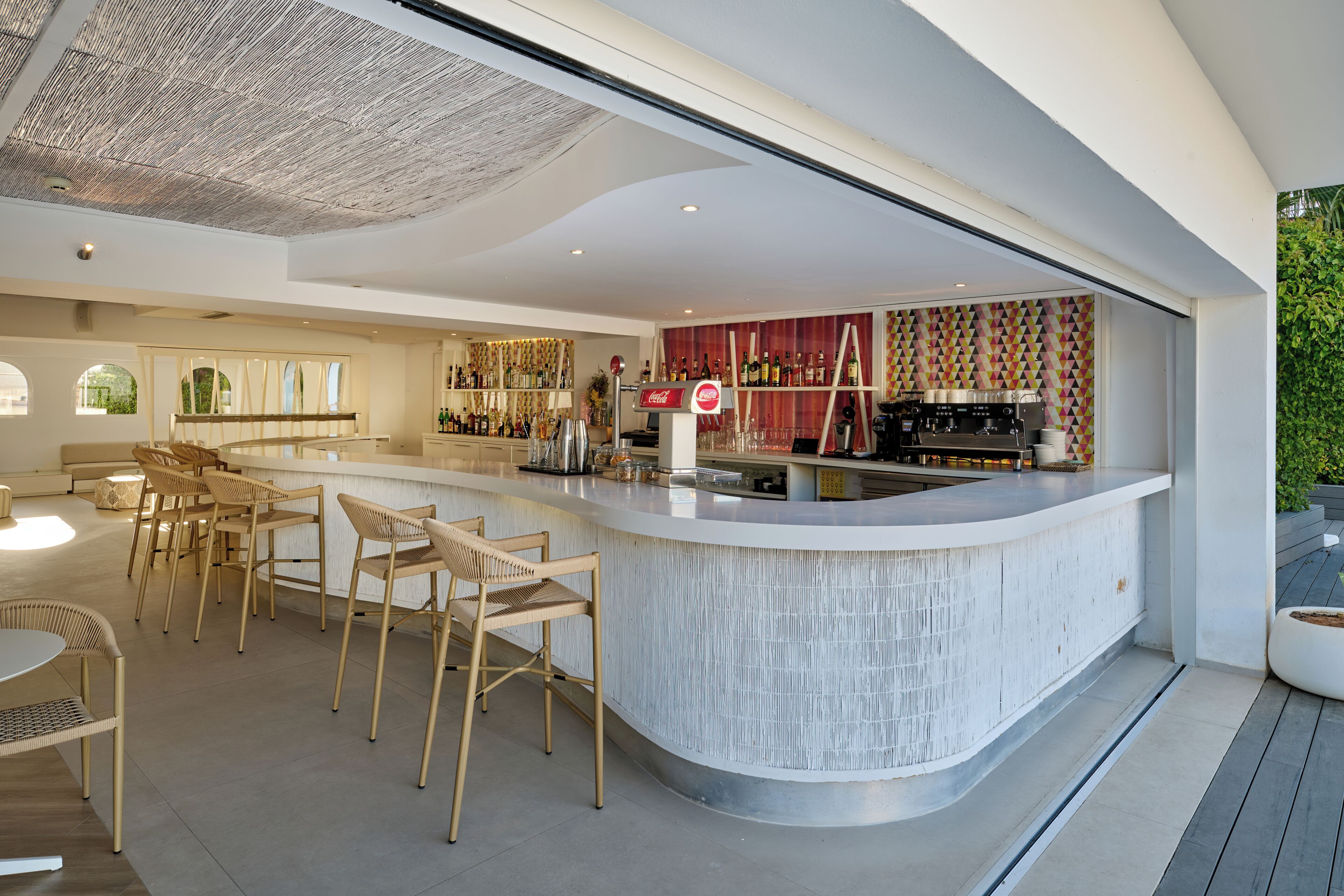 Zona de bar moderna con una barra curva, taburetes y una variedad de botellas y vasos.