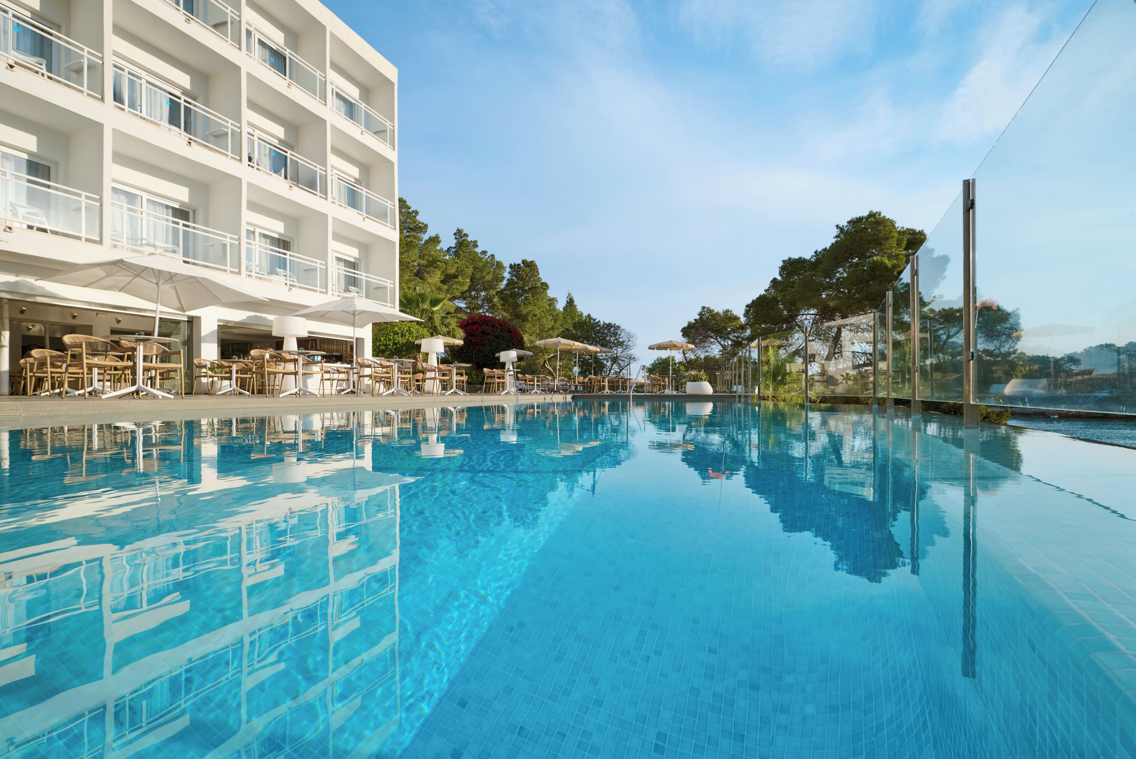 A clear swimming pool with lounge chairs and umbrellas, surrounded by a building with multiple balconies.