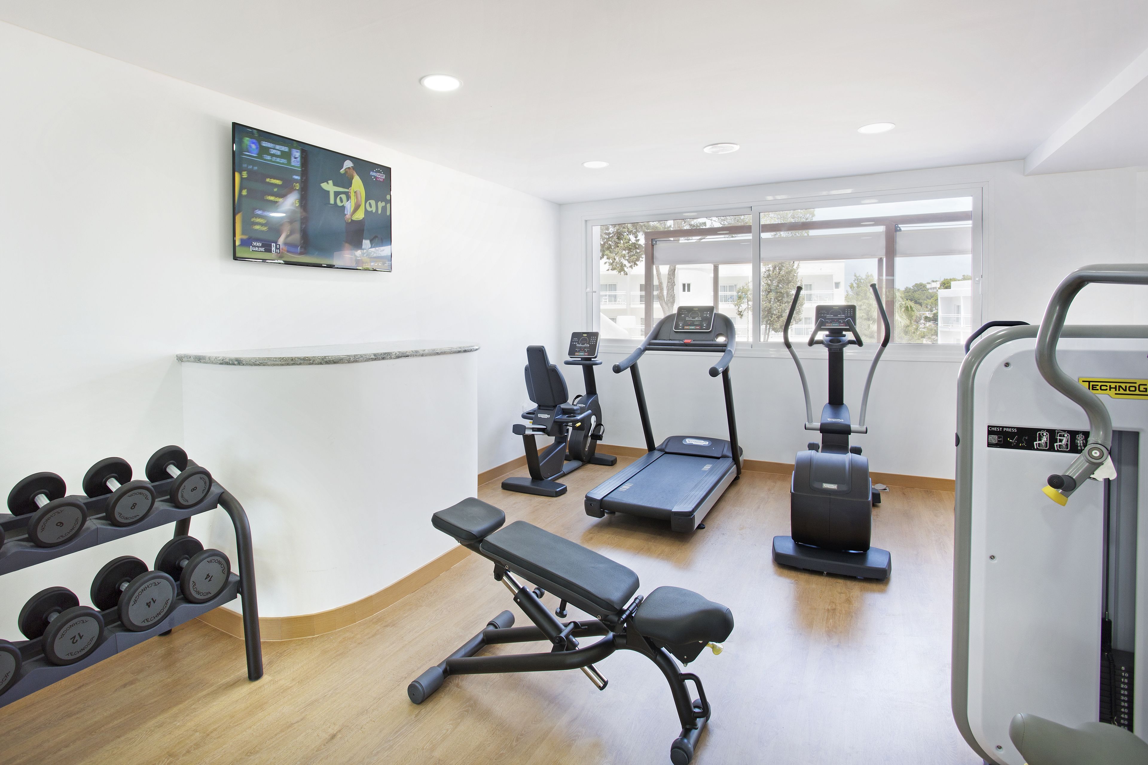 A gym with a treadmill, elliptical, bench press, and dumbbell rack.