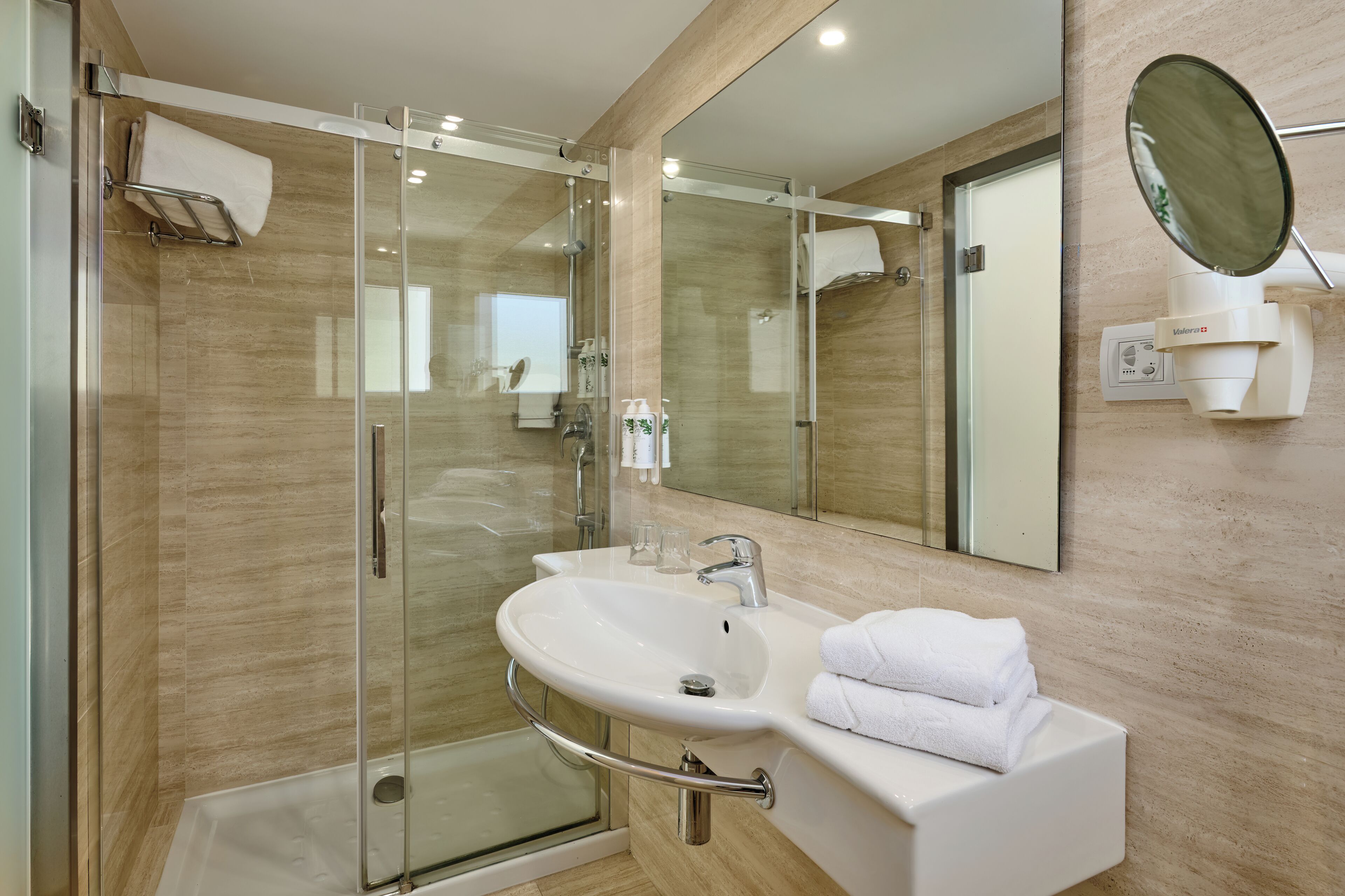 A modern bathroom with a glass-enclosed shower, a white sink, and a large mirror.