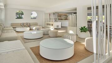 A modern living room with a sofa, ottomans, a coffee table, a bookshelf, and a potted plant.
