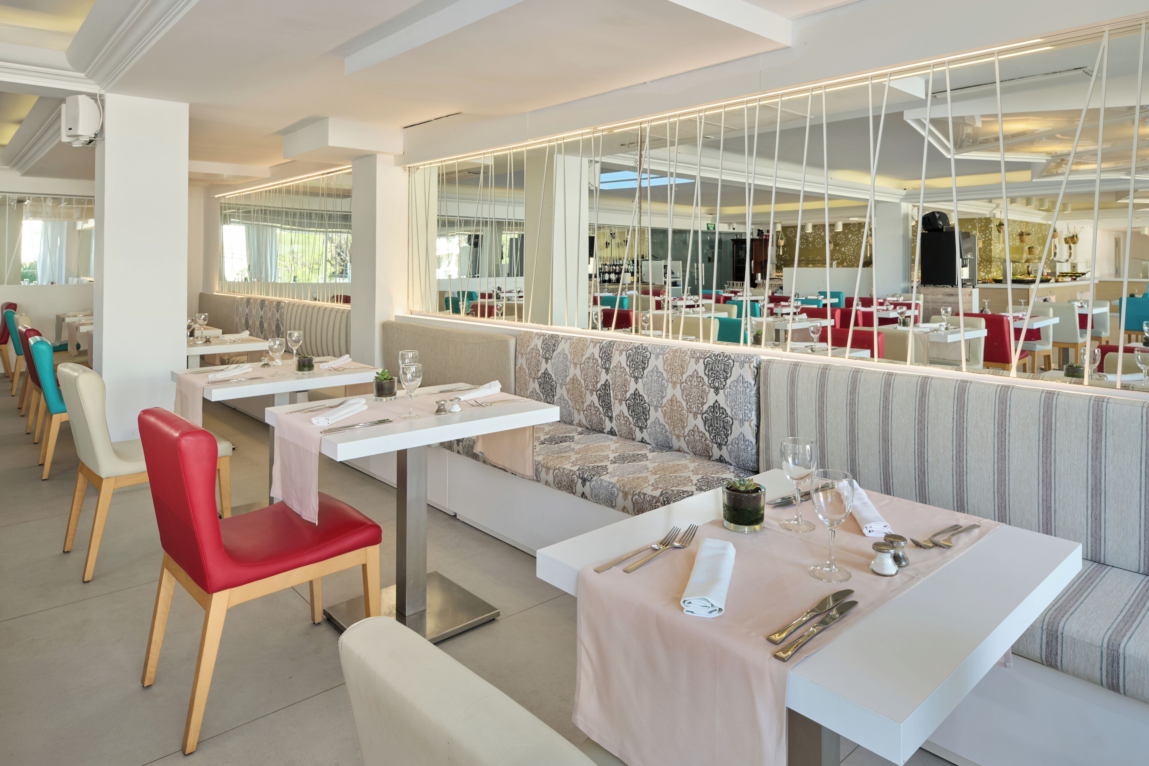Un restaurante con mesas blancas, sillas rojas y cojines estampados.