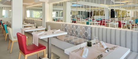 Un restaurante con mesas blancas, sillas rojas y cojines estampados.