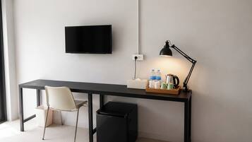 A modern hotel room with a desk, chair, TV, desk lamp, and a trash bin.